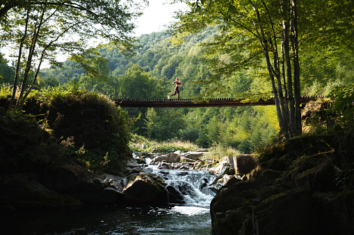 Woman running across bridge in nature.