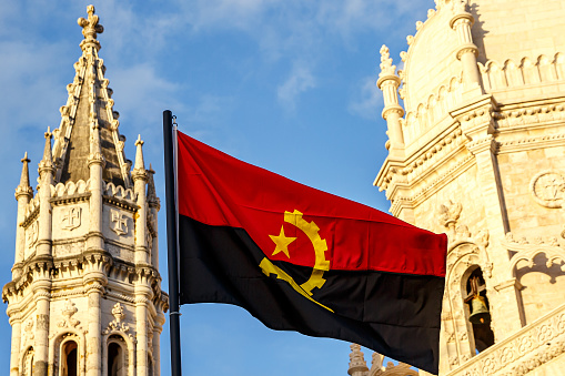 Angola flag waving in front of a blue sky and old building