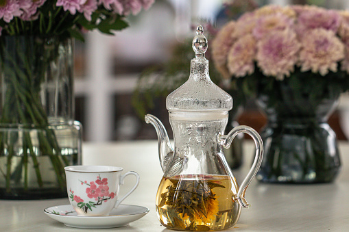 Teapot and cup with blooming tea flower and pink Chrysanthemum flowers in glass vase on table.