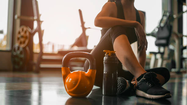 Fitness woman Relaxing after exercise with a whey protein and dumbbell placed beside the gym.Relaxing after training.beautiful young woman looking away while sitting  at gym. stock photo