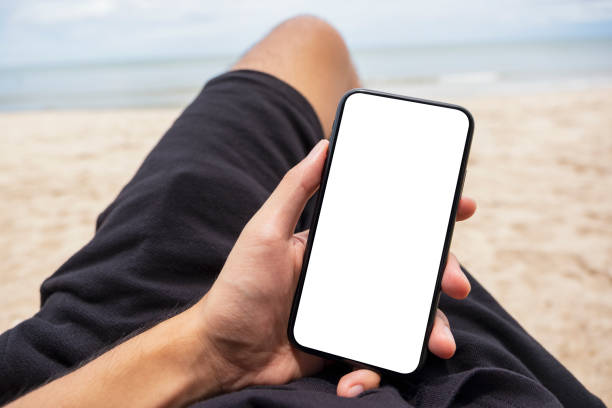 istock a man's hand holding black mobile phone with blank desktop screen while lying down on beach chair 1175381058