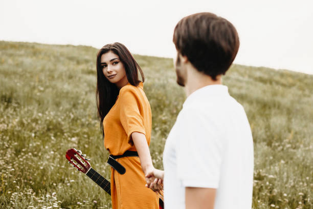 hermosa joven caminando de la mano con su novio en un campo. - couple old fashioned hipster holding hands fotografías e imágenes de stock