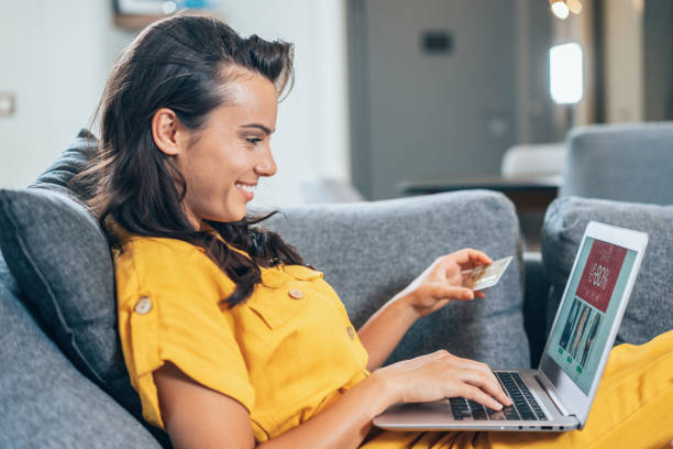 Online shopping Young beautiful woman shopping online on the sofa at home using laptop and credit card clothing store credit card stock pictures, royalty-free photos & images