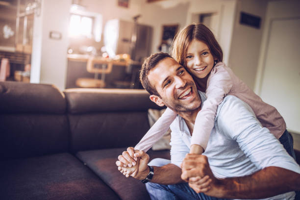 Happy single father having fun with his small daughter at home. Happy single father and daughter having fun in the living room. Girl is looking at camera. father and daughter stock pictures, royalty-free photos & images