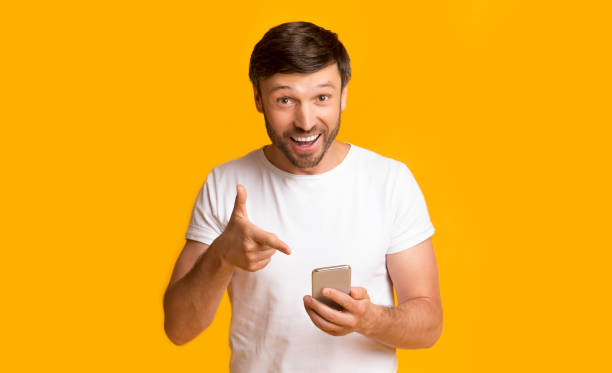 istock Man Pointing At Phone Over Yellow Background In Studio 1175416241