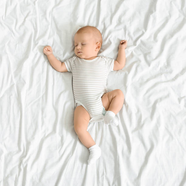 adorabile neonato che sonnecchia su una coperta bianca con le braccia alzate - sleeping baby foto e immagini stock