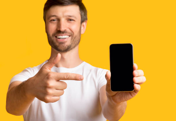 istock Man Holding Smartphone Pointing Finger At Screen, Yellow Background 1175416706