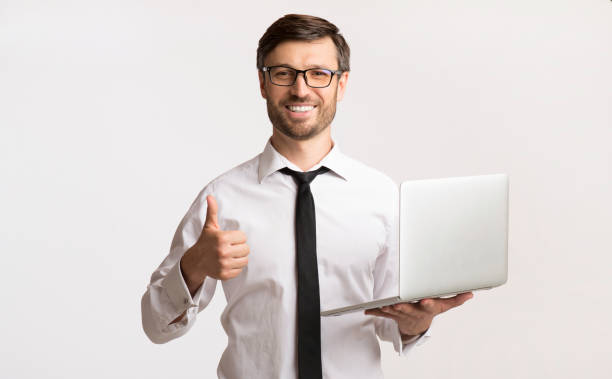 businessman holding laptop gesturing thumbs-up over white background - thumbs up business people isolated imagens e fotografias de stock