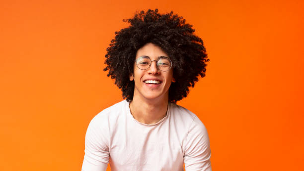 Happy millennial black guy laughing on orange background Sincere emotions. Happy millennial black guy with bushy hair laughing on orange panorama background black orange audio stock pictures, royalty-free photos & images