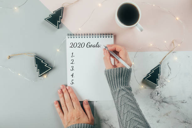 istock Happy New Year 2020. Woman's hand writing 2020 Goals in notebook decorated with Christmas decorations on the tricolor background. Top view, flat lay 1175417687