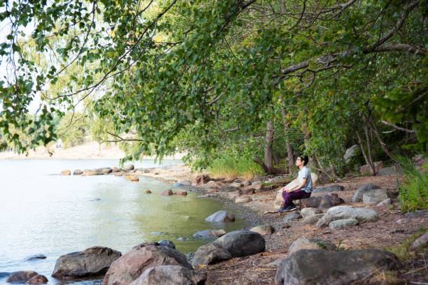A man sitting on a rock by a lake, meditating.
