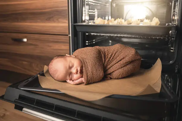 Photo of Newborn baby is lying on the oven tray with a muffins