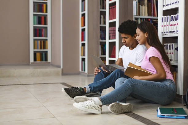 istock Young couple of black students studying on floor in library 1175433971