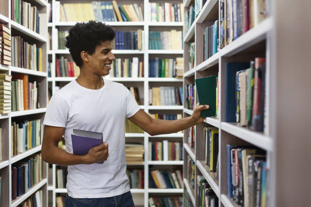 istock Handsome black guy looking for book on bookshelves in library 1175434246