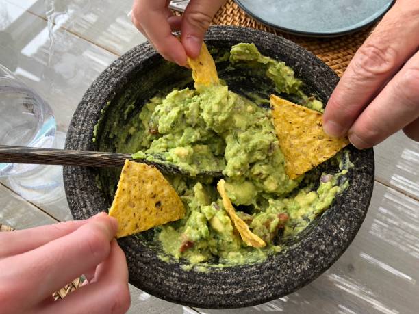 Guacamole dip and tortilla chips Three hands holding tortilla chips and dipping them in guacamole dipping stock pictures, royalty-free photos & images