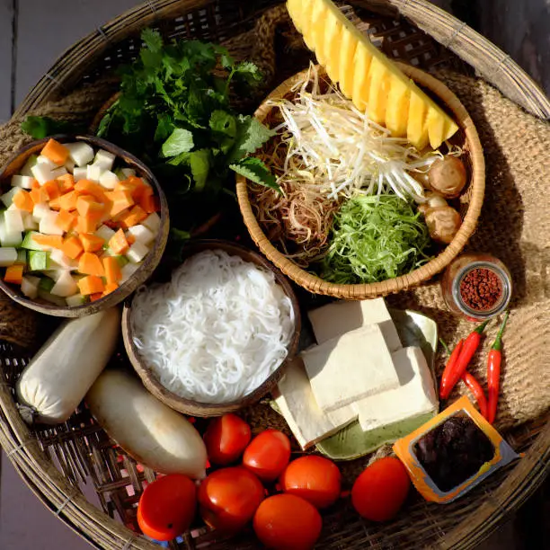 Prepare raw materials for vegan rieu noodle soup or vegetarian bun rieu, a traditional Vietnamese food with tomato, tofu, tamarind, pine apple, sausage, herbs, vegetable and rice vermicelli
