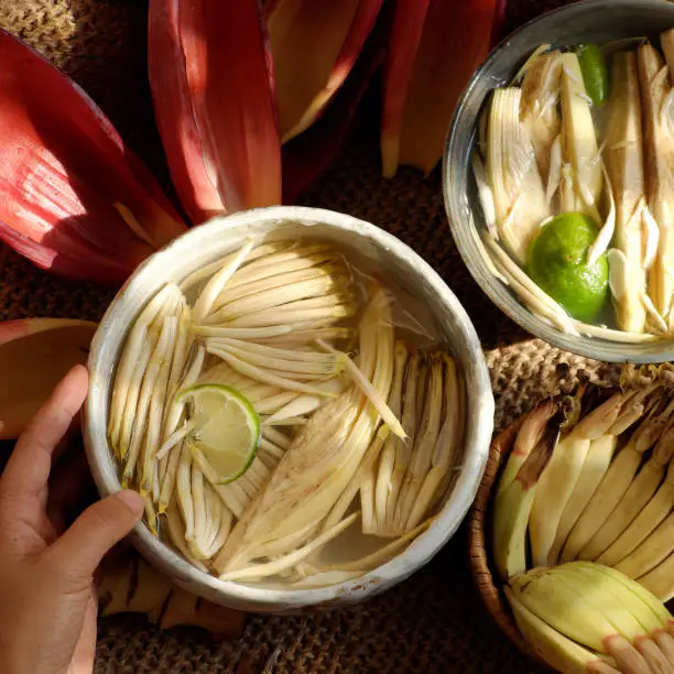 Top view prepare ingredients for vegan food  from banana flower, woman hand take young bananas, soaked in lemon water, this blossom can make many vegetarian dish, healthy eating with fiber