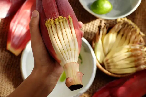 Top view prepare ingredients for vegan food  from banana flower, woman hand take young bananas, soaked in lemon water, this blossom can make many vegetarian dish, healthy eating with fiber