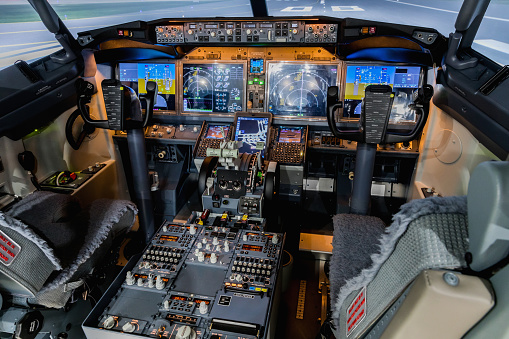 Cabin of a large airliner. View of cockpit control and seats in simulator. Switches and dials visible in the background.