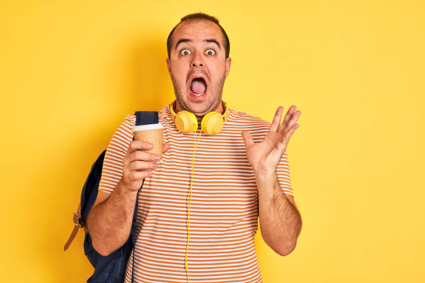 istock Student man wearing backpack headphones drinking coffee over isolated yellow background very happy and excited, winner expression celebrating victory screaming with big smile and raised hands 1175438416