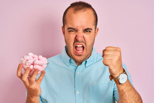 istock Young man holding bowl with marshmallows standing over isolated pink background annoyed and frustrated shouting with anger, crazy and yelling with raised hand, anger concept 1175439917