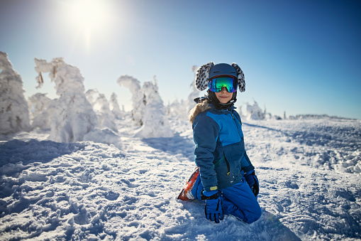 Portrait of a cute boy wearing ski helmet with funny ears. There are frozen tips of trees visible in the background.
Nikon D850