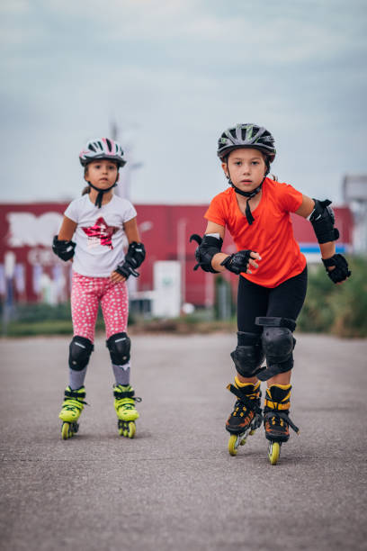 Two cute girls roller skating Two young girls roller skating together on the street together. elbow pad stock pictures, royalty-free photos & images