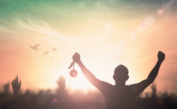Winner concept Silhouette champion hand holding gold medal reward against blurred sport crowd autumn sunset background sports team event stock pictures, royalty-free photos & images
