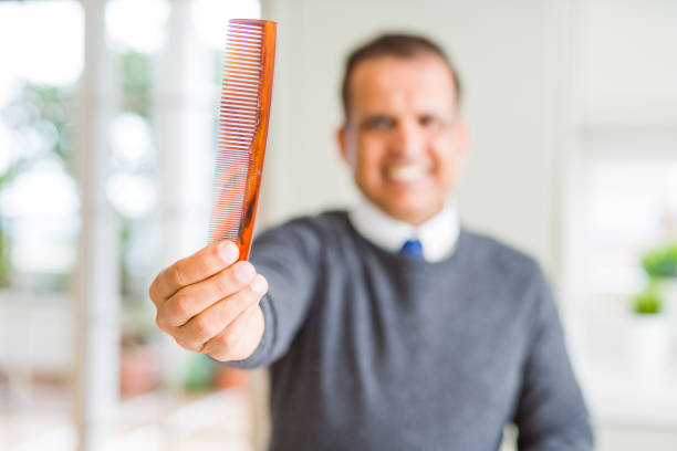 Middle age man holding and showing hair comb while smiling to the camera