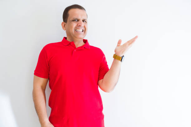 istock Middle age man wearing red t-shirt over white wall smiling cheerful presenting and pointing with palm of hand looking at the camera. 1175444840