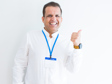 Middle age business man wearing ID card over white background smiling with happy face looking and pointing to the side with thumb up.