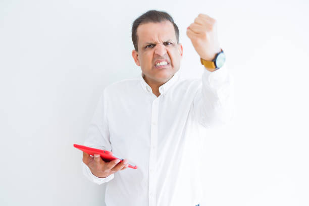 istock Middle age man using digital table over white wall annoyed and frustrated shouting with anger, crazy and yelling with raised hand, anger concept 1175447672