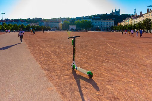 Overview of the Place Bellecour, It is one of the largest open squares in Europe. In the middle is an equestrian statue of King Louis XIV by François-Frédéric Lemot. Tourists are walking across the square with a motorised push scooter in the foreground. A typical summer day in Lyon, France