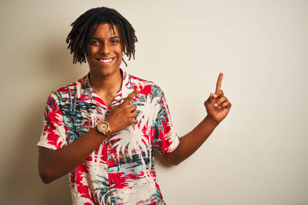 istock Afro man with dreadlocks on vacation wearing summer shirt over isolated white background smiling and looking at the camera pointing with two hands and fingers to the side. 1175449086