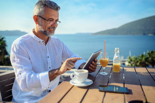 homme s'asseyant à un café travaillant sur la tablette numérique - reading beach e reader men photos et images de collection