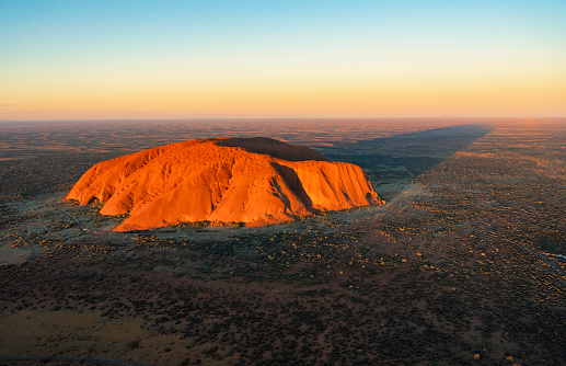 Northern Territory, Australia - August 08, 2019: Evening sun shines down on the magnificence of Uluru, in Australia's Northern Territory. A place sacred to the local Anangu people and adored by holidaymakers, it's also a UNESCO World Heritage site. Elevated view from a helicopter.