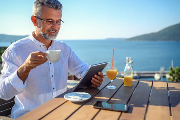 homme s'asseyant à un café travaillant sur la tablette numérique - reading beach e reader men photos et images de collection