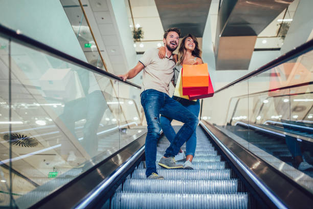 istock Happy young couple with shopping bags going down by escalator 1175452370