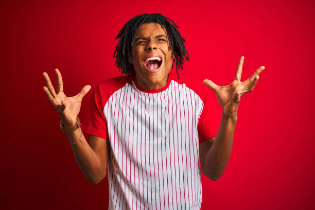 istock Afro man with dreadlocks wearing striped t-shirt standing over isolated red background celebrating mad and crazy for success with arms raised and closed eyes screaming excited. Winner concept 1175452919