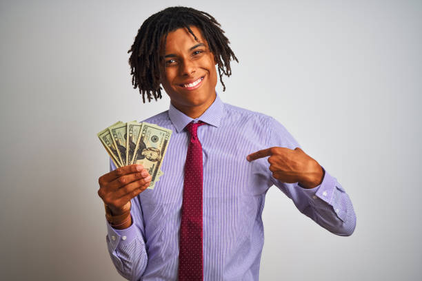 istock Afro american businessman with dreadlocks holding dollars over isolated white background with surprise face pointing finger to himself 1175452980