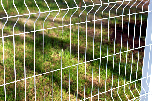 white mesh fence on the street separates the asphalt road from the grass lawn