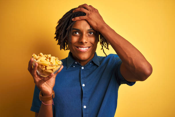 istock Afro american man with dreadlocks holding pasta macaroni over isolated yellow background stressed with hand on head, shocked with shame and surprise face, angry and frustrated. Fear and upset for mistake. 1175456455