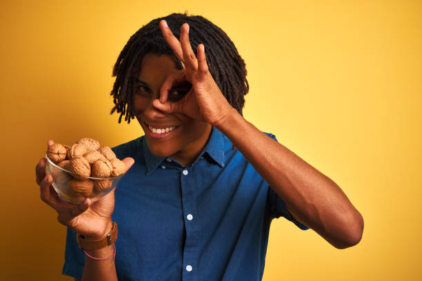 istock Afro american man with dreadlocks eating walnuts over isolated yellow background with happy face smiling doing ok sign with hand on eye looking through fingers 1175456533