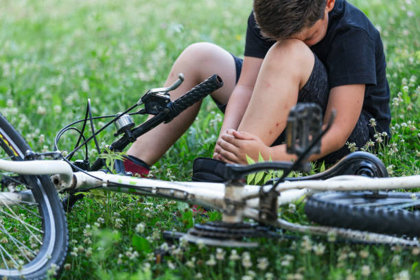 concept bike accident, młody chłopak z bólem stawów kolanowych po rowerze na rowerze w parku. kostka boli po upadku roweru. uraz dziecka - ludzki limb zdjęcia i obrazy z banku zdjęć