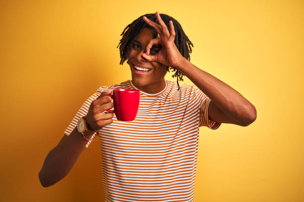istock Afro american man with dreadlocks drinking a cup of coffee over isolated yellow background with happy face smiling doing ok sign with hand on eye looking through fingers 1175459712