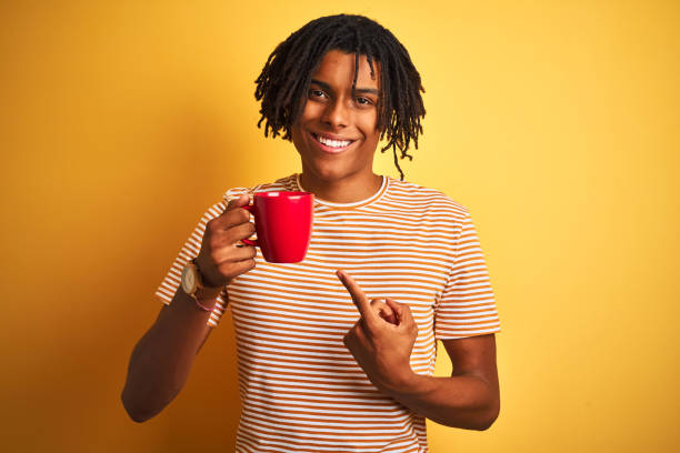 istock Afro american man with dreadlocks drinking a cup of coffee over isolated yellow background very happy pointing with hand and finger 1175459773