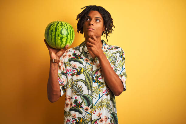 istock Afro american man with dreadlocks holding watermelon over isolated yellow background serious face thinking about question, very confused idea 1175460928
