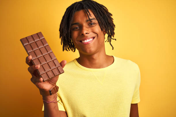 istock Afro american man with dreadlocks eating chocolate bar over isolated yellow background with a happy face standing and smiling with a confident smile showing teeth 1175465245