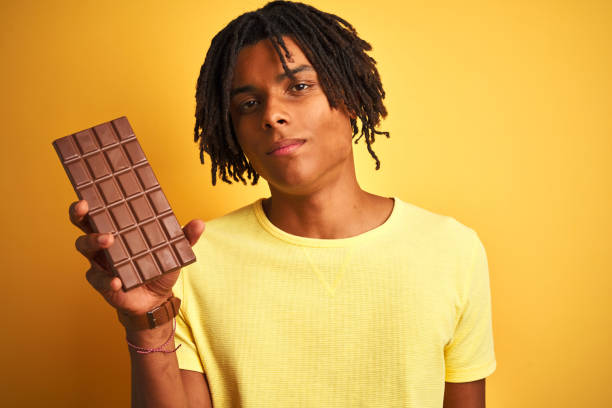 istock Afro american man with dreadlocks eating chocolate bar over isolated yellow background with a confident expression on smart face thinking serious 1175465277