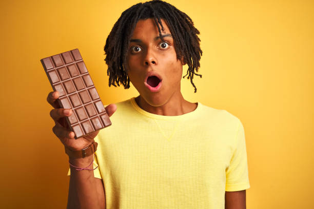 istock Afro american man with dreadlocks eating chocolate bar over isolated yellow background scared in shock with a surprise face, afraid and excited with fear expression 1175465329